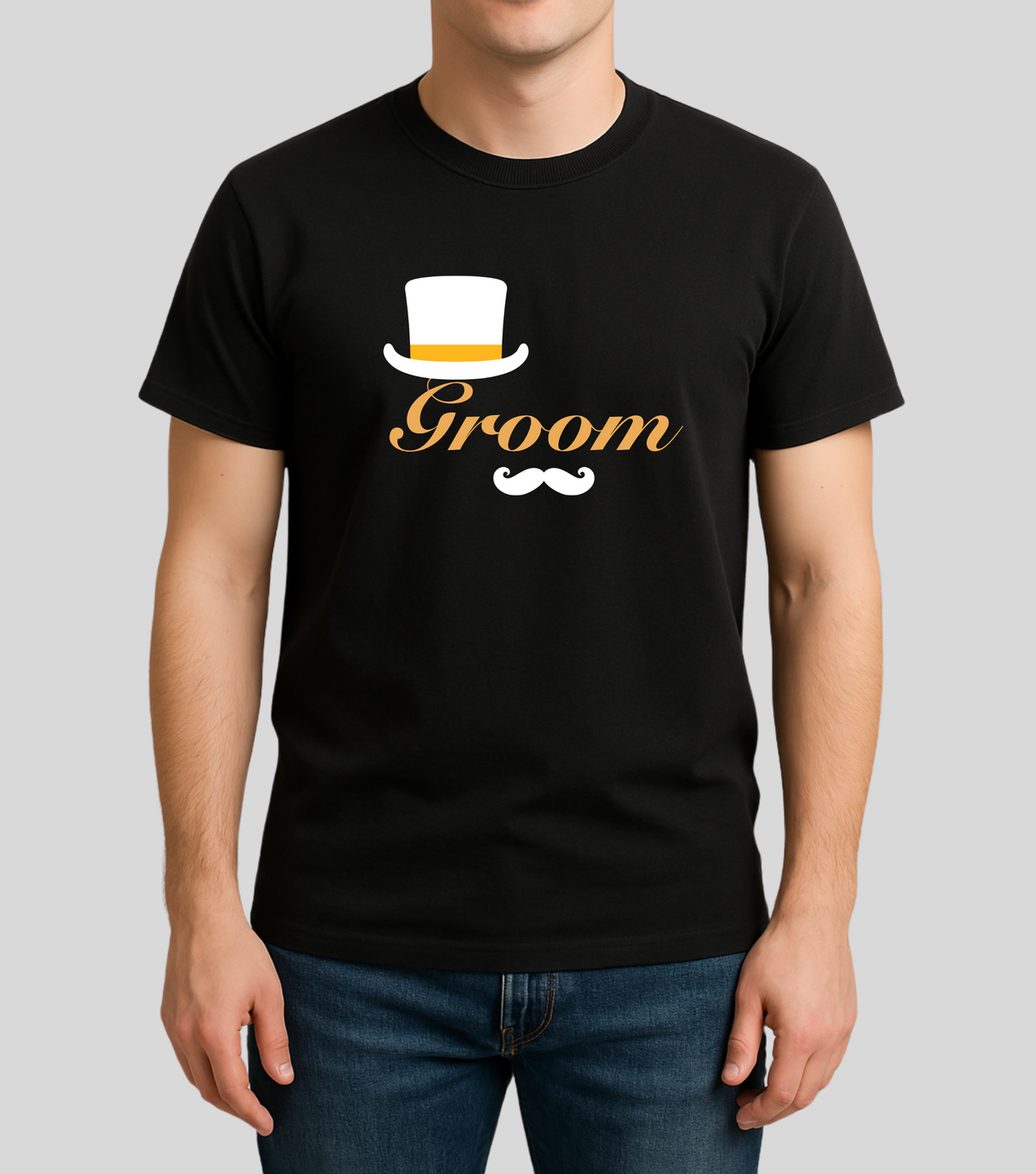 A man wearing a black short-sleeve t-shirt with a 'Groom' graphic on the chest, featuring a white top hat, white mustache, and gold script text, paired with blue jeans against a light gray background.
