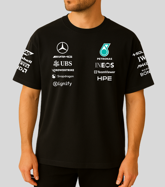 A man wearing a black Mercedes Petronas Formula 1 team t-shirt with various sponsor logos printed in white and teal on the front and sleeves.